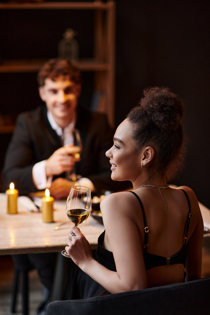 heureuse femme afro-américaine tenant un verre de vin pendant la date avec l'homme sur la Saint-Valentin - Photo, image