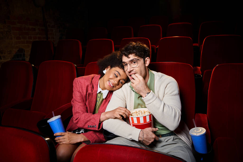 bell'uomo con gli occhiali che mangia popcorn accanto alla sua ragazza afro-americana al cinema in data - Foto, immagini