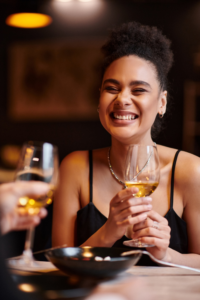 joyful african american woman smiling and holding glass of wine during date on Valentines day - Photo, Image