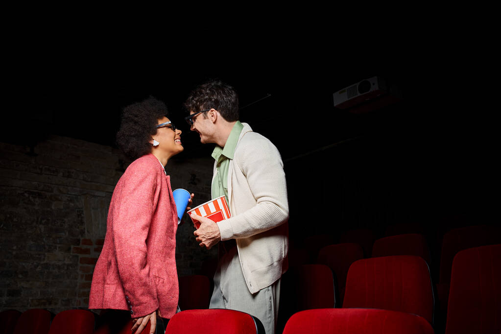 Веселая молодая многорасовая пара счастливо улыбается друг другу на свидании в кино, в День Святого Валентина - Фото, изображение