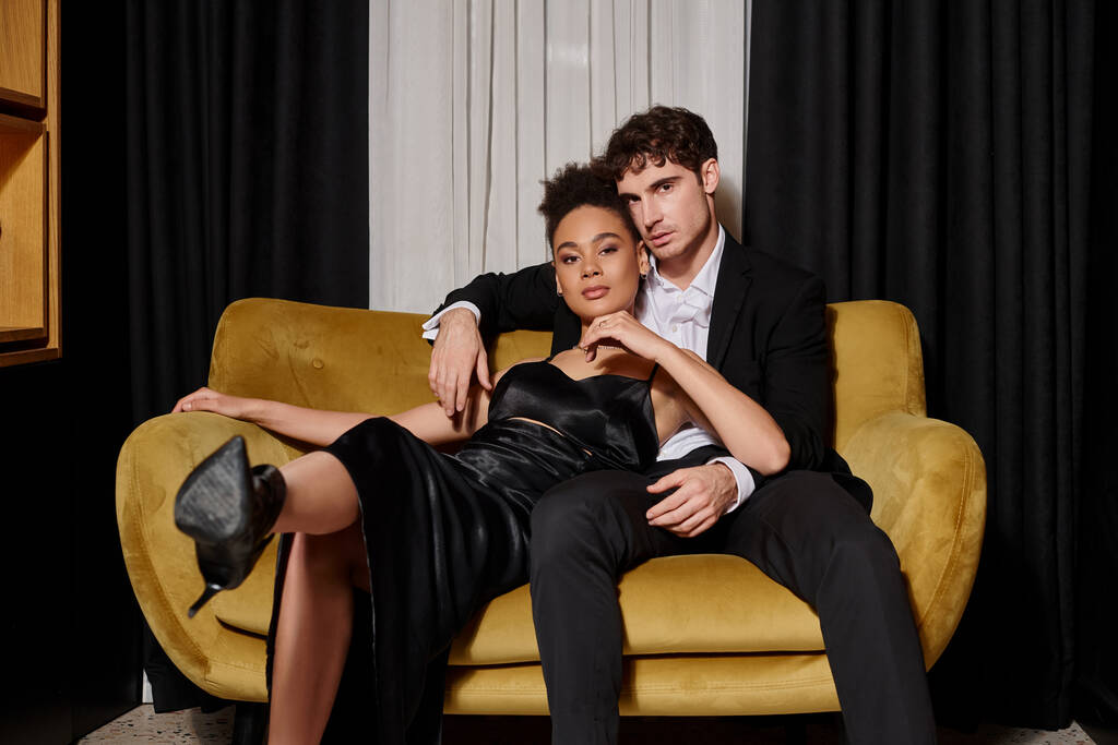 jovem mulher afro-americana em vestido e homem bonito em terno elegante sentados juntos no sofá - Foto, Imagem
