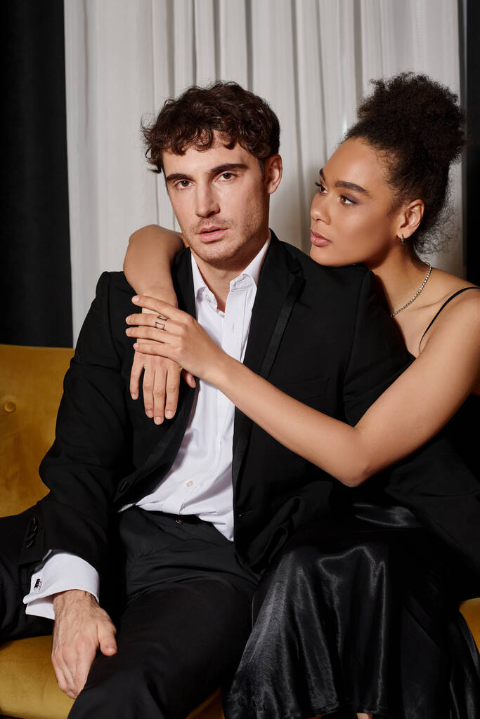 attractive african american woman in black  dress embracing good looking man in suit on velvet sofa - Photo, Image