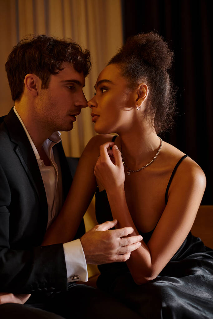 інтимний момент, красива мультикультурна пара в чорному вбранні дивиться один на одного ввечері - Фото, зображення