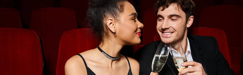 багаторасова пара в елегантному вбранні, клінкеруючи шампанські окуляри і дивлячись один на одного, банер - Фото, зображення