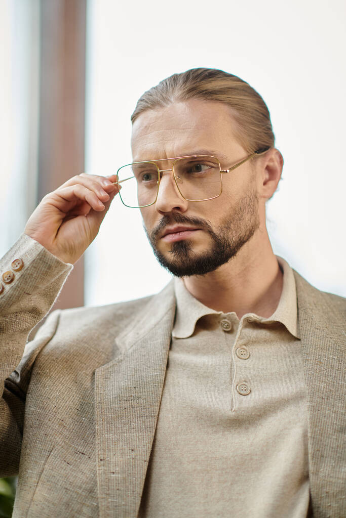 pohledný vůdce s nasbíranými vlasy v brýlích v elegantním sofistikovaném obleku pózování atraktivně - Fotografie, Obrázek