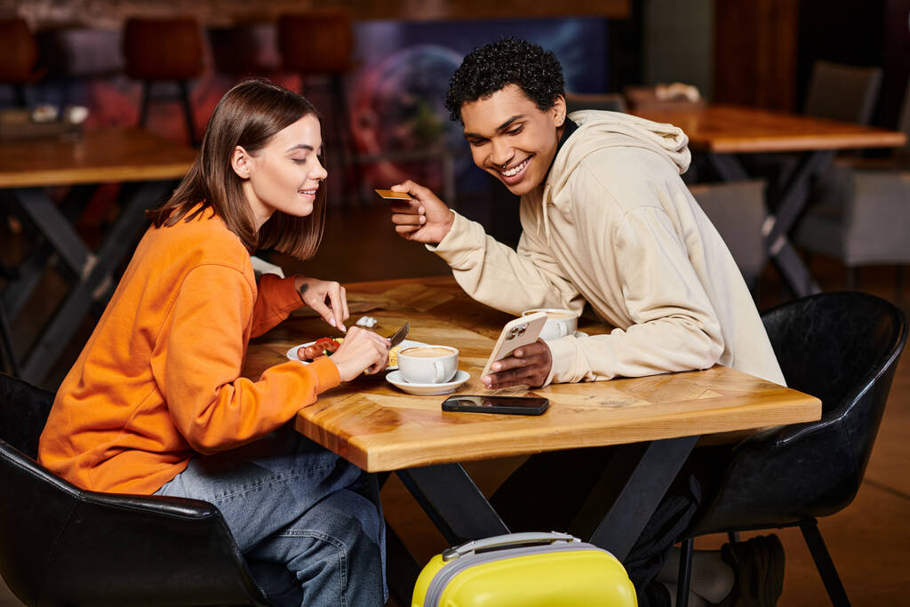 Разнообразная пара, занимающаяся контентом на смартфоне в кафе и обедающая, делающая онлайн покупки - Фото, изображение