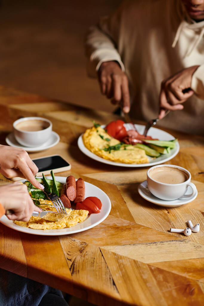 joven pareja diversa disfrutando del desayuno en la cafetería, tortilla y salchichas cerca de la taza de café - Foto, Imagen