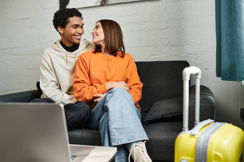 позитивна багатоетнічна пара розслабляється на дивані у своїй стильній вітальні біля ноутбука на столі - Фото, зображення