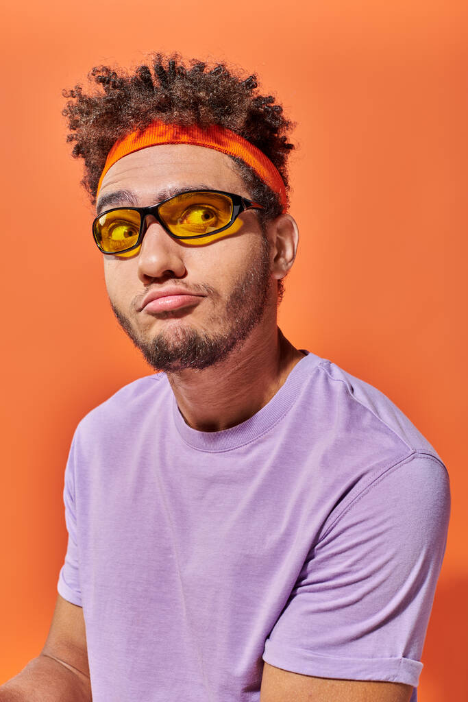 confused african american fella in eyeglasses and headband looking away on orange background - Photo, Image