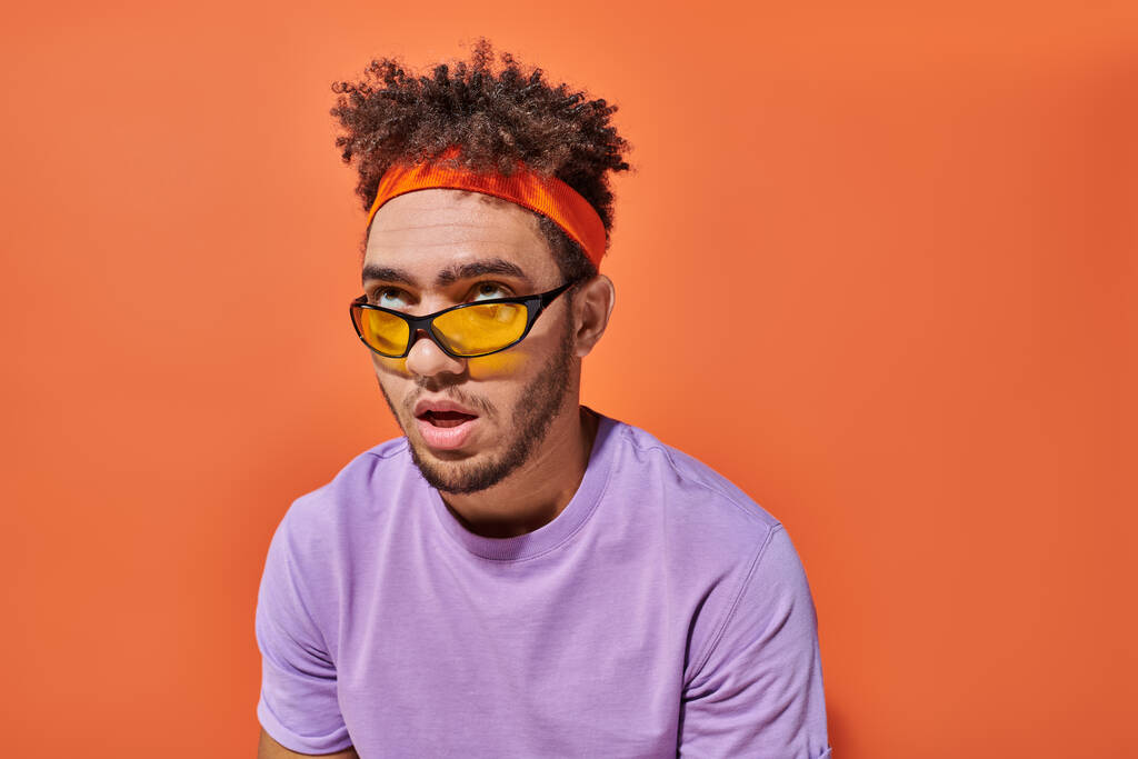 homme afro-américain ennuyé dans les lunettes et bandeau rouler les yeux sur fond orange - Photo, image