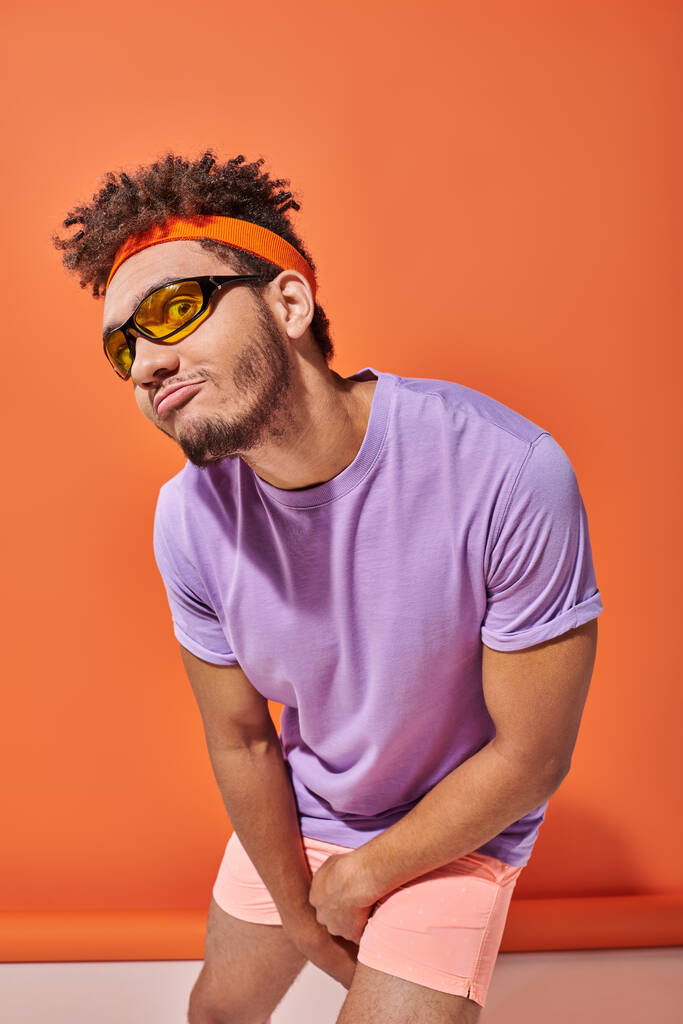 funny african american man in eyeglasses and headband pouting lips on orange background - Photo, Image