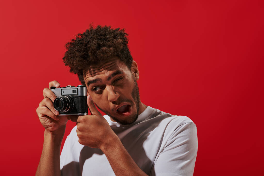 vicces afro-amerikai fotós nézi keresőt, miközben lő a piros háttér - Fotó, kép