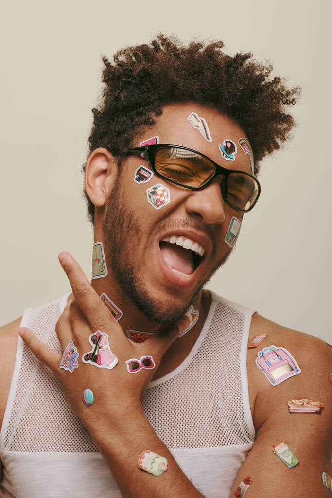 expressive african american fella in sunglasses with trendy stickers on face on grey background - Photo, Image