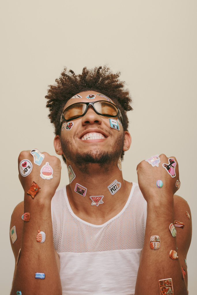 glimlachende jonge Afro-Amerikaanse man in zonnebril met trendy stickers op gezicht op grijze achtergrond - Foto, afbeelding