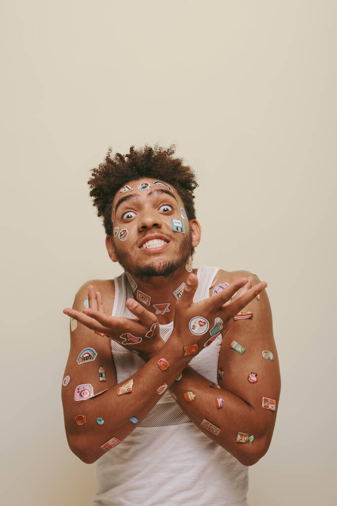 емоційний афроамериканський чоловік з наклейками на обличчі жестикулює на сірому фоні, хіпстер - Фото, зображення