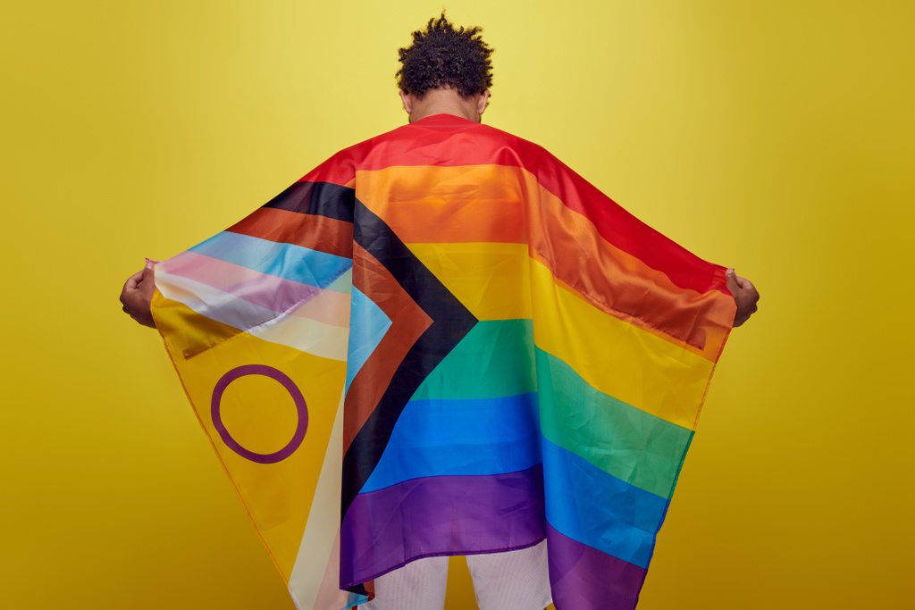 back view of african american guy holding rainbow lgbt flag on yellow background, pride month - Photo, Image