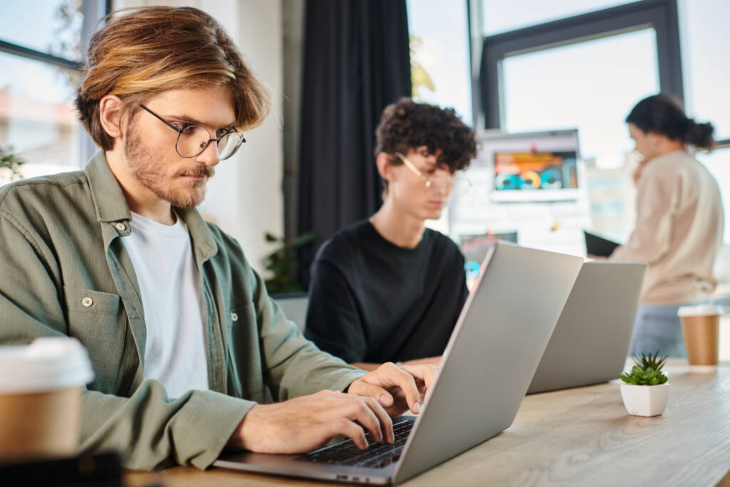 Fiatal startup csapat mélyen összpontosított, miközben dolgozik a laptopok a modern coworking térben, férfiak a 20-as években - Fotó, kép