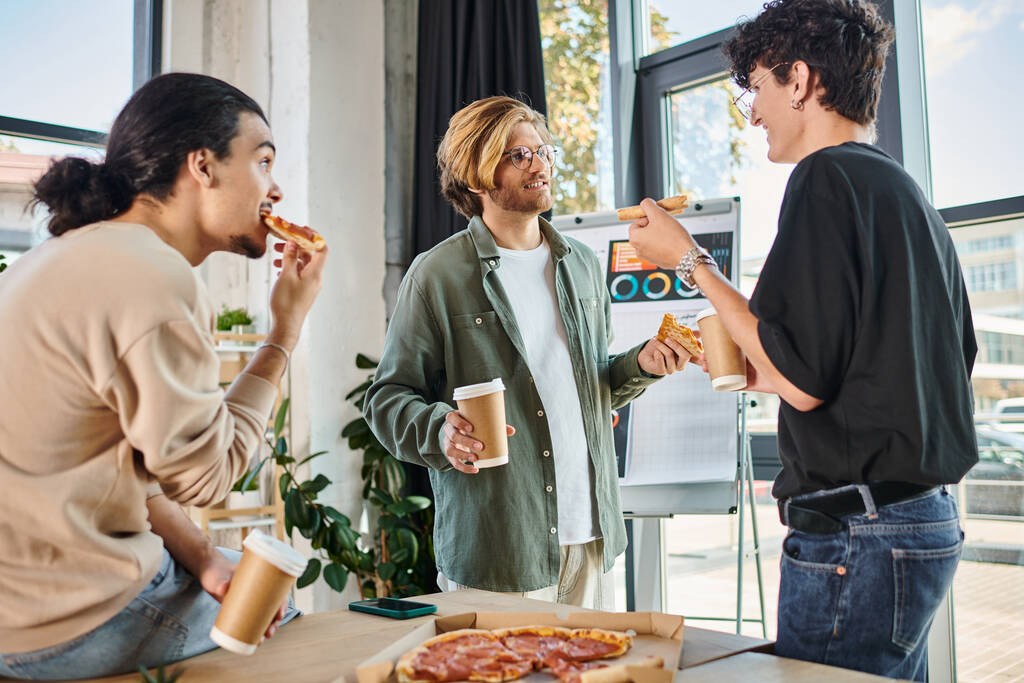 hombres jóvenes comiendo pizza y charlando en un ambiente agradable y relajado, equipo durante el almuerzo - Foto, imagen