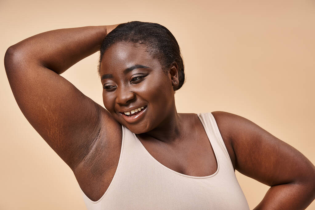 Confident plus size african american woman smiling with hand behind head on beige background - Photo, Image