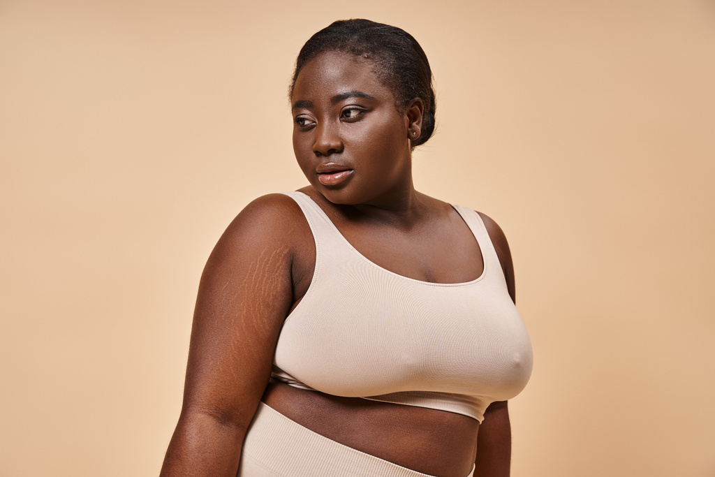 Plus la taille femme afro-américaine en sous-vêtements beige posant judicieusement sur fond beige - Photo, image