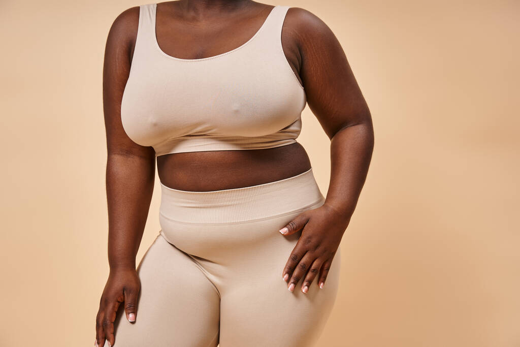 bijgesneden plus size Afrikaans amerikaanse vrouw in ondergoed poseren op beige achtergrond, lichaam positief - Foto, afbeelding
