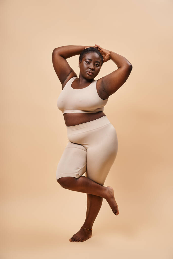 Graceful plus size african american woman in beige attire posing against a matching backdrop - Photo, Image