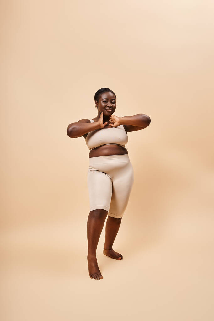 smiling plus size african american model in beige attire posing against a matching backdrop - Photo, Image