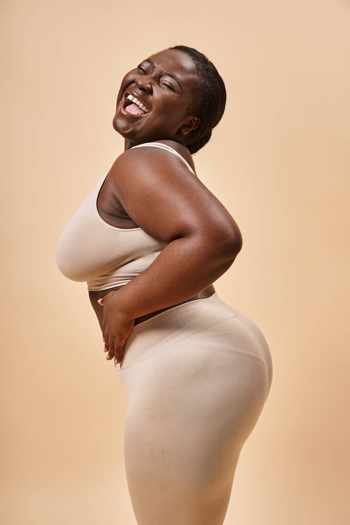 cheerful plus size african american woman posing against matching backdrop, body positive - Photo, Image