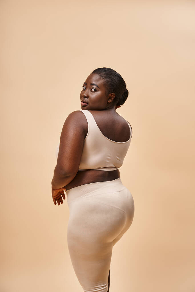 young plus size african american woman in beige underwear posing against matching backdrop - Photo, Image