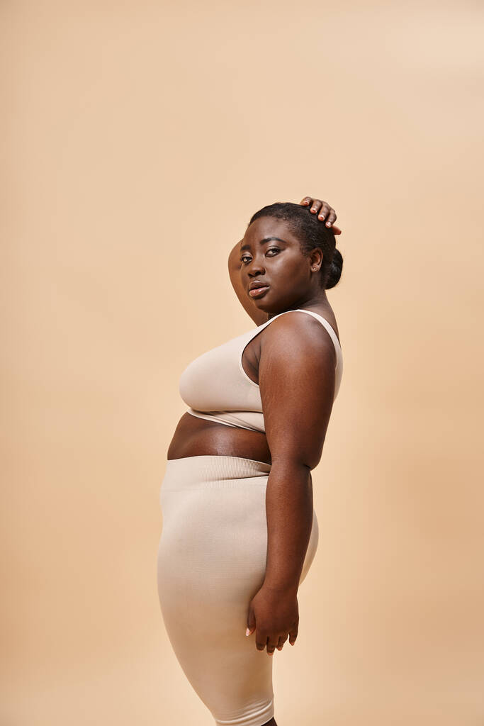 молодые плюс размер африканская американская женщина в нейтральном цвете нижнего белья позирует на фоне сопоставления - Фото, изображение
