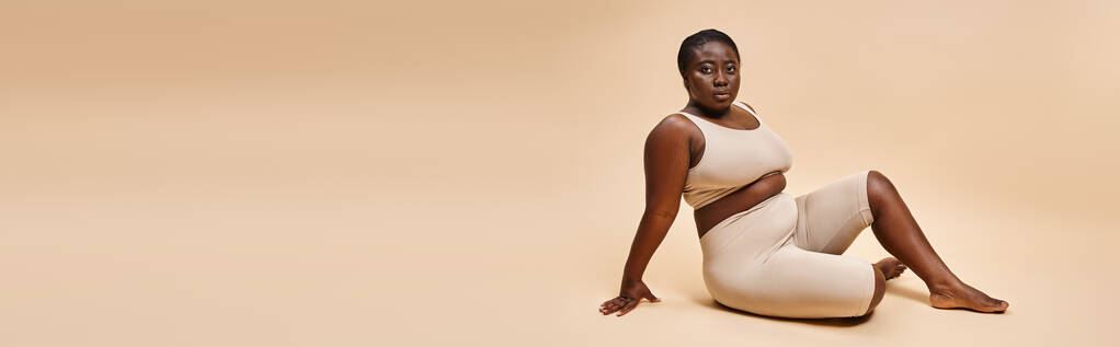 plus size afroamericana giovane donna in biancheria intima beige posa sullo sfondo corrispondente, banner - Foto, immagini