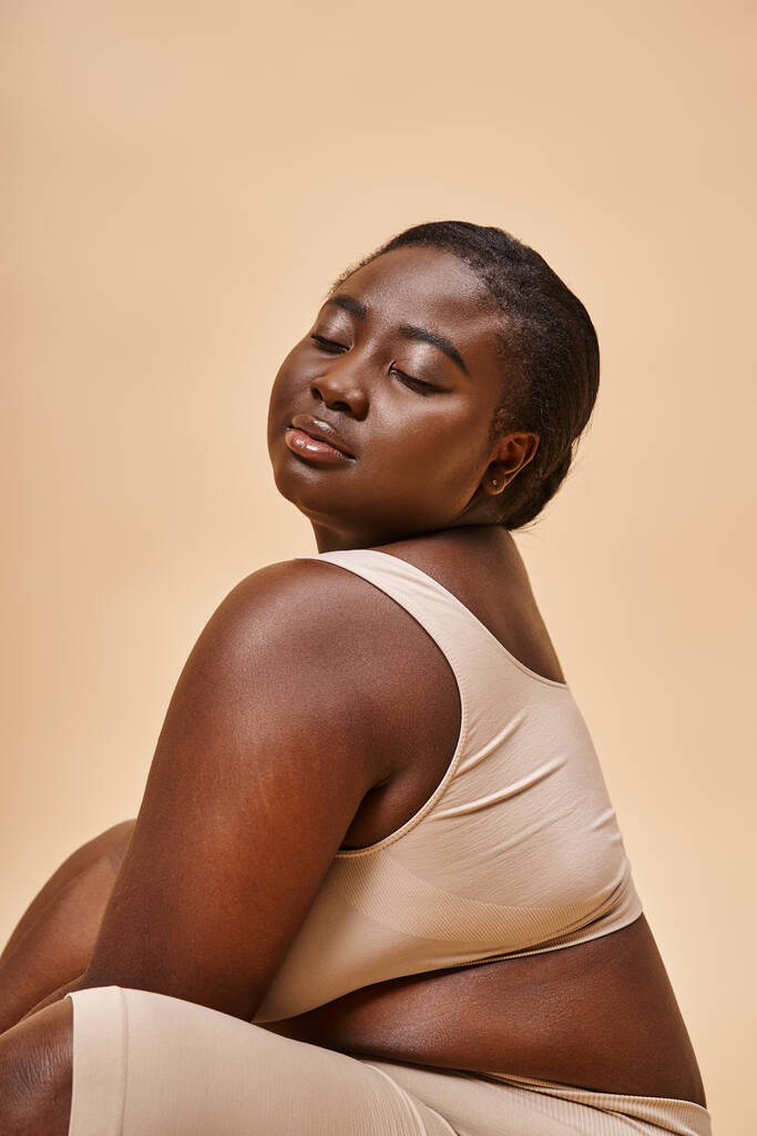 body positive, plus size african american woman in beige underwear posing against matching backdrop - Photo, Image