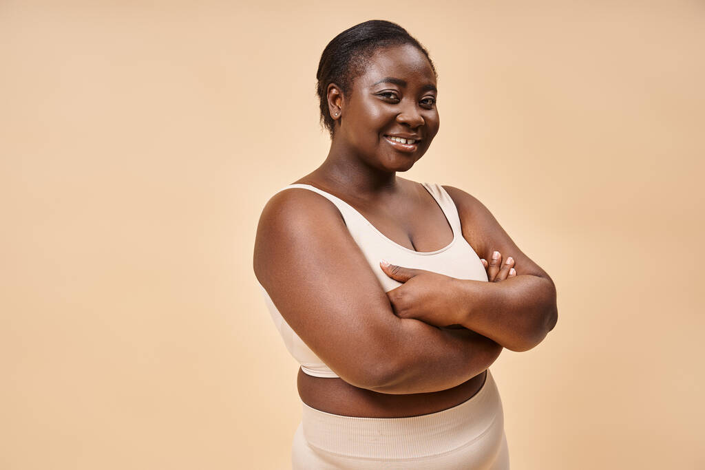 glückliche Plus-Size-Frau in beiger Unterwäsche posiert im Studio, Körper positiv und Selbstwertgefühl - Foto, Bild