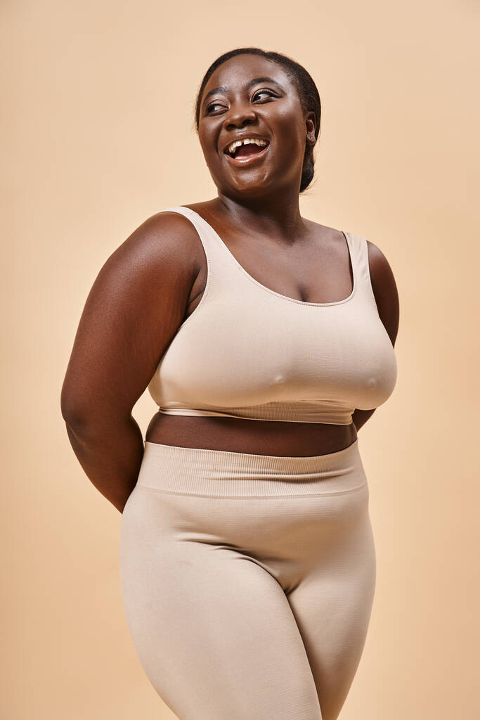 happy plus size woman in beige underwear laughing in studio, body positive and self esteem - Photo, Image