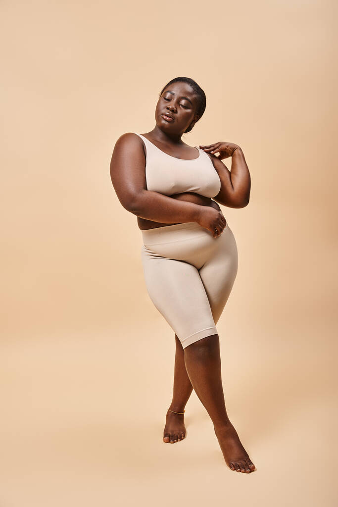 plus size vrouw in ondergoed poseren op beige achtergrond, lichaam positief en gevoel van eigenwaarde concept - Foto, afbeelding