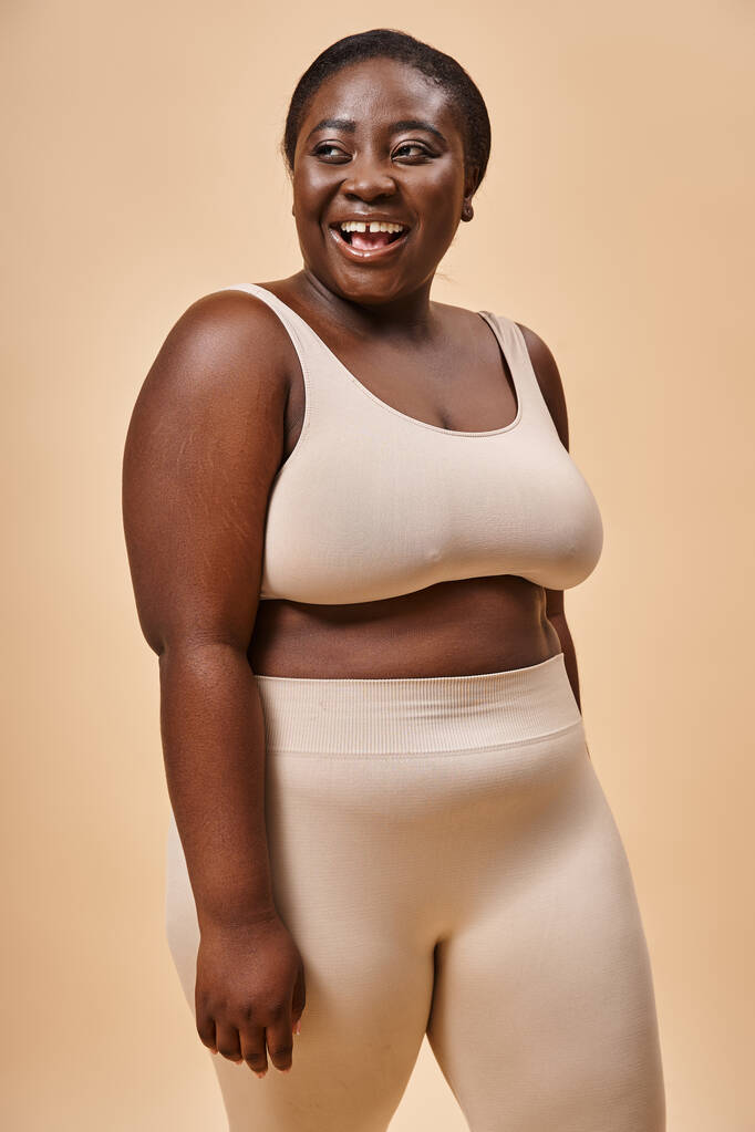 joyful plus size woman in beige underwear laughing and looking away, body positive and self esteem - Photo, Image