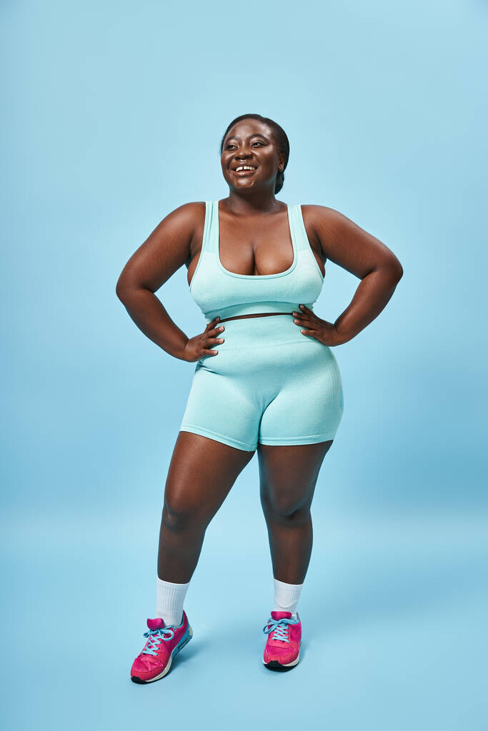 幸せなプラスサイズのアフリカ系アメリカ人女性のブルースポーツウェアとマッチングバックドロップ上のヒップ - 写真・画像