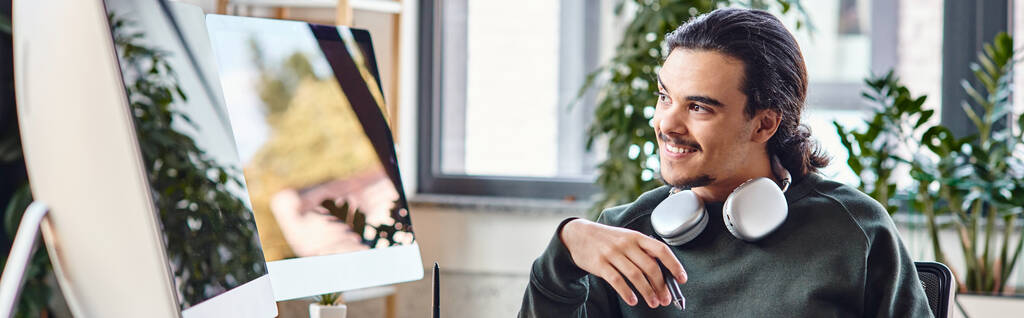 άνθρωπος με στυλό και καφέ χαμογελώντας και κοιτάζοντας οθόνη στο γραφείο μετά την παραγωγή, πανό - Φωτογραφία, εικόνα