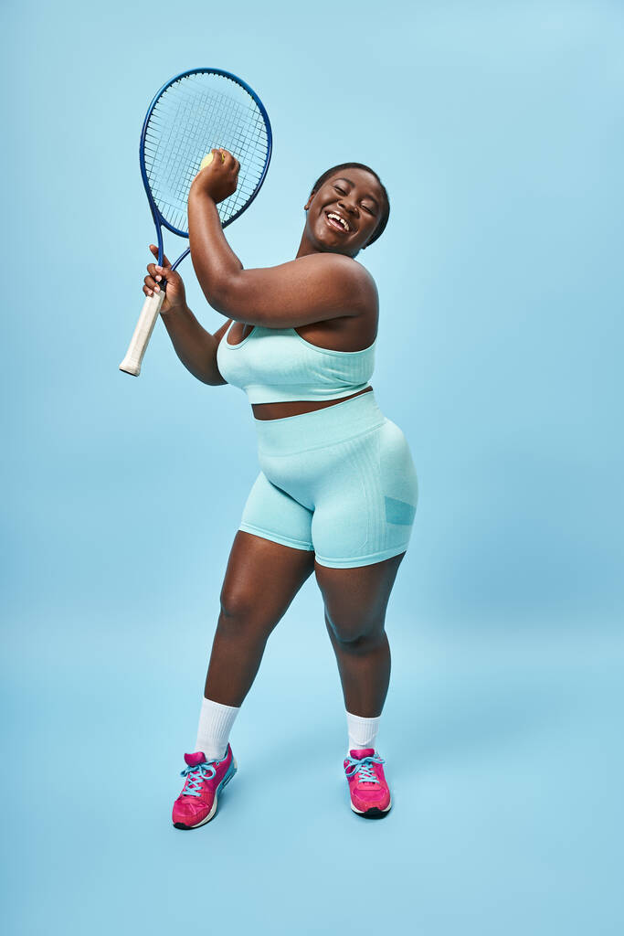 plus size Afroamerykanka amerykańska kobieta gotowa do gry w tenisa na niebieskim tle, body positive i sport - Zdjęcie, obraz