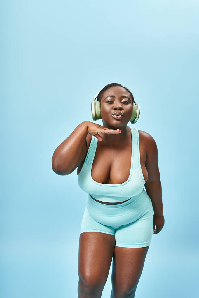 plus size african american woman in sportswear listening music in headphones and pouting lips - Photo, Image