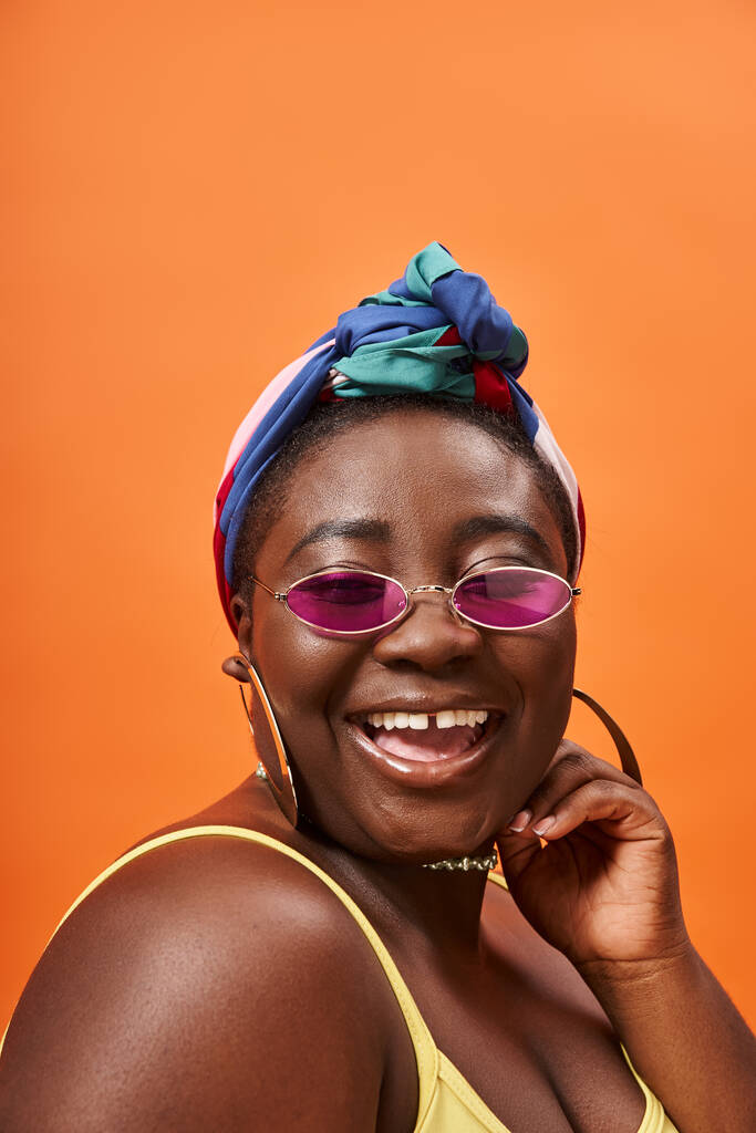 cheerful and plus size african american woman in headscarf and trendy sunglasses on orange - Photo, Image