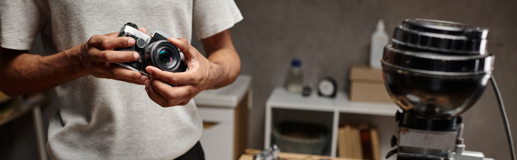 hombre negro recortado Sujetando intencionadamente una cámara analógica mientras está de pie en un laboratorio de fotos, pancarta - Foto, imagen
