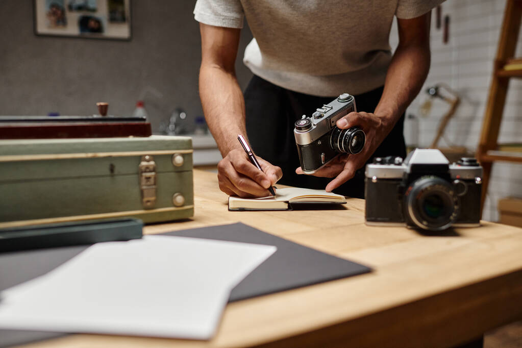 geschnittener afrikanisch-amerikanischer Fotograf in Schrift vertieft, seine analoge Kamera im Fotostudio haltend - Foto, Bild