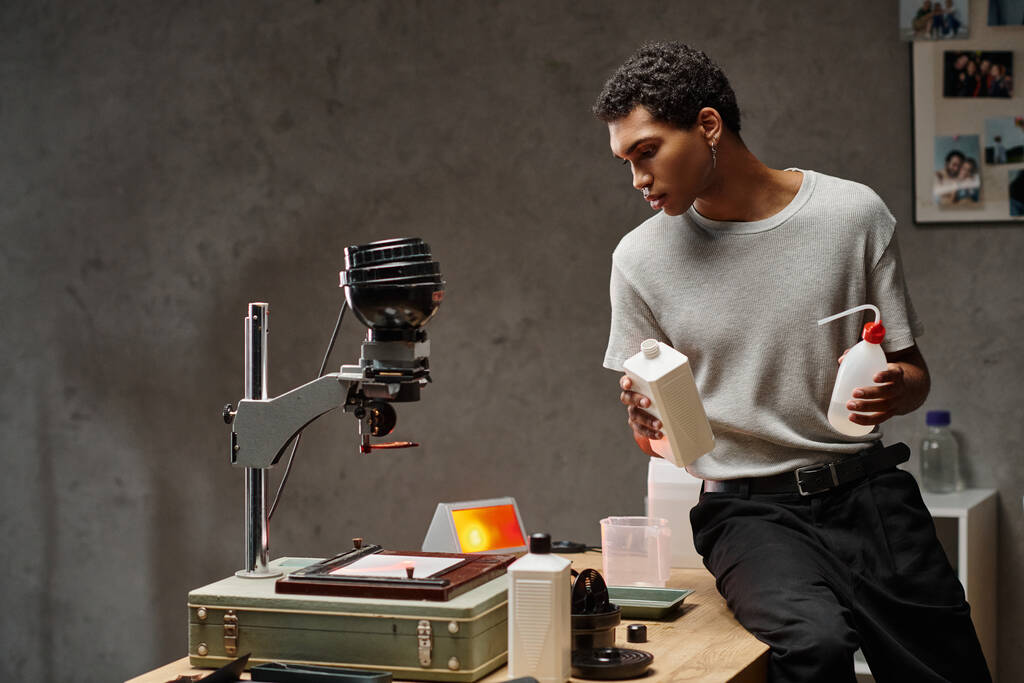 Сфокусований афроамериканський чоловік ретельно вимірює фотохімічні речовини в добре організованій темній кімнаті - Фото, зображення