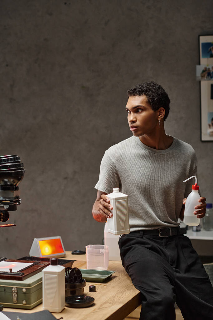 молодий афроамериканський чоловік ретельно вимірює хімічні речовини фотоплівки в добре організованій темній кімнаті - Фото, зображення