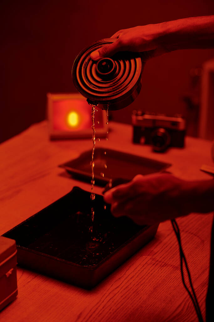 photo recadrée du photographe versant le liquide développeur pour le traitement du film, chambre noire rouge - Photo, image
