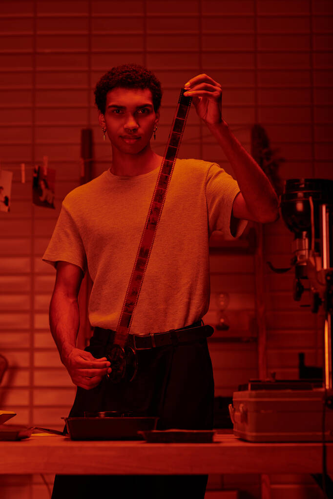 fokussierte afrikanisch-amerikanische Kerl spult Film in Vorbereitung auf die Entwicklung in der Dunkelkammer mit rotem Licht - Foto, Bild