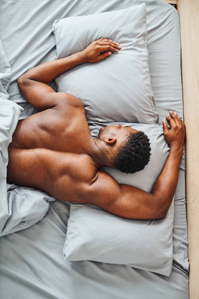 Modern yatak odasındaki gri yatak odasında uyuyan Afrikalı Amerikalı genç adamın en iyi görüntüsü. - Fotoğraf, Görsel