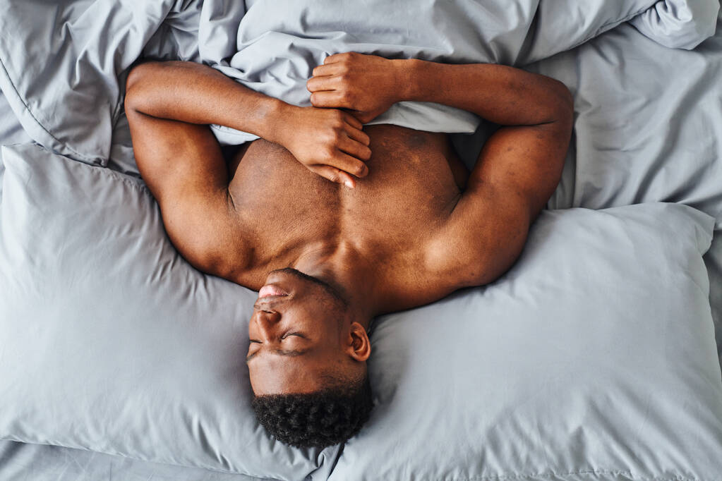 Güçlü vücutlu Afro-Amerikan adam, evinde rahat bir yatak hayal ediyor. - Fotoğraf, Görsel
