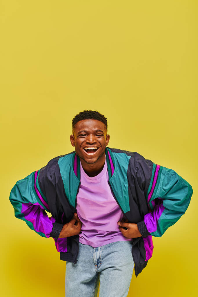 黄色い背景のカメラで笑うファッショナブルなカジュアルな服装で興奮するアフリカ系アメリカ人男性 - 写真・画像